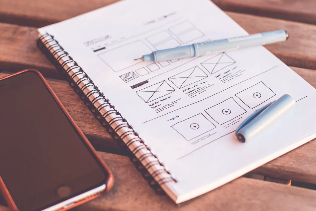 Wireframe sketches of website pages in a notebook beside a phone